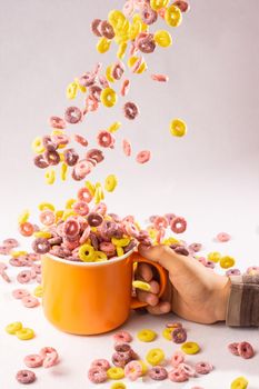 colored cereal rings falling into an orange cup held by a child's hand on white background with side lighting