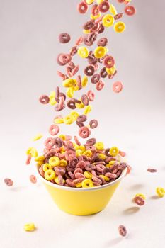 colored cereal rings falling into a yellow bowl on white background with soft side lighting