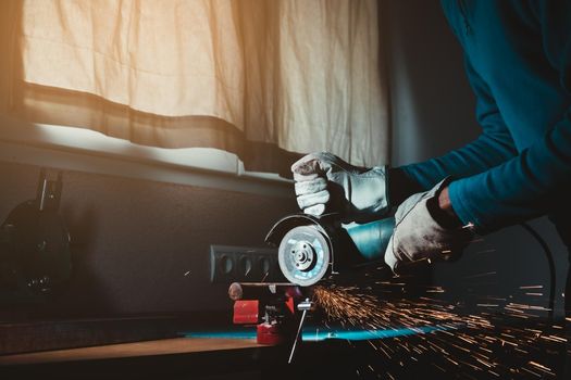 man hands with gloves holding a circular saw cutting an iron bar with burning orange sparks jumping with side lighting