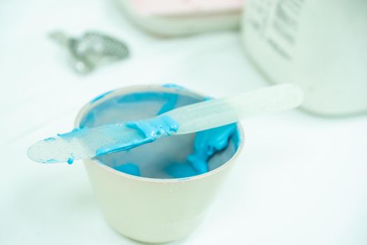 white bowl with blue alginate paste for dental impressions with plastic trowel for mixing