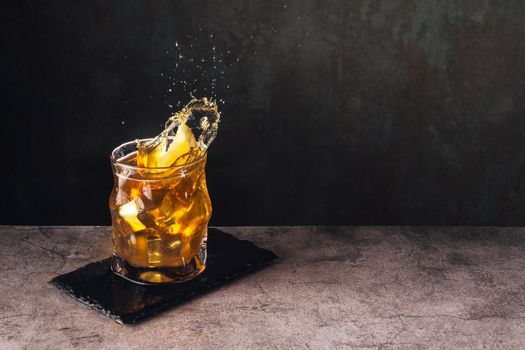 splash of tea with ice and lemon on stone surface with dark background and high speed splash