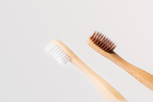 two diagonal wooden toothbrushes one with white bristles and the other brown on light background