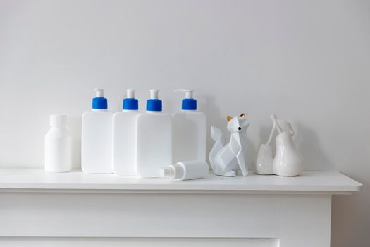White bottles with a blue dispenser with shampoo, conditioner, cream and liquid soap, figurines stand on a shelf in the bathroom. Place for text.