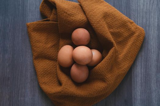 five fresh eggs on a rustic wooden table and wrapped in kitchen towel