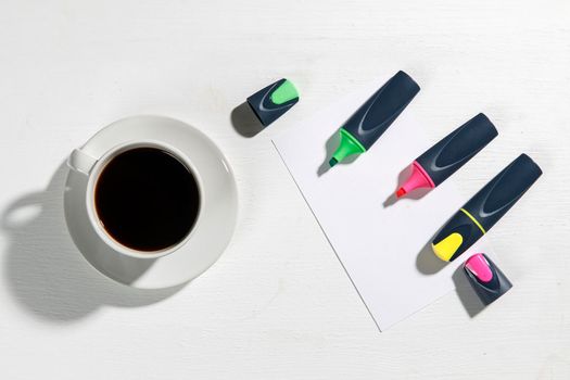 Workplace. Multicolored markers with a piece of paper and a cup of coffee on a beige table