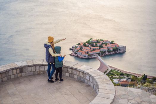 Mom and son travelers on background of beautiful view of the island of St. Stephen, Sveti Stefan on the Budva Riviera, Budva, Montenegro. Travel to Montenegro concept. Travel around Montenegro in spring, winter, autumn.