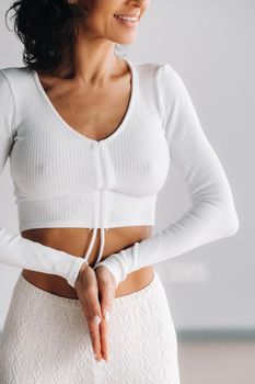 a female yogi in white clothes stands with her hands clasped at the bottom meditating in the yoga hall.