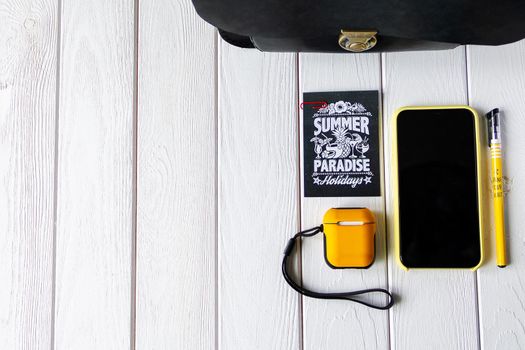 Black bag, headphones, smartphone, yellow pen and paper on wooden background