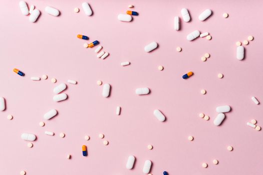 tablets and capsules of medicines of different colors and sizes randomly scattered on a pink background occupying the entire image