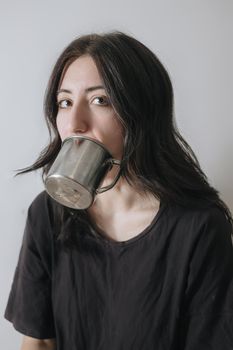 Young woman with a cup of tea at the window during quarantine wearing face mask worried about the new lifestyle. Anxiety, stress, mental health, crisis, depression, psychology therapy.