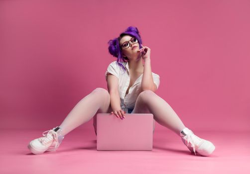 the sexy girl with glasses and purple hair with a laptop on a pink background