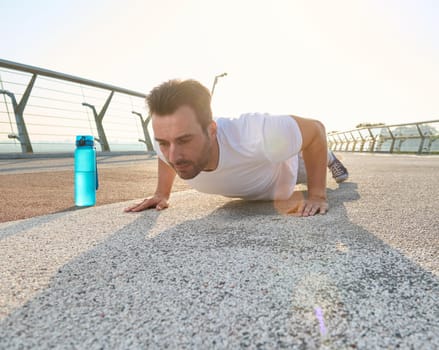Middle aged Caucasian man, athlete, sportsman performing push-up exercise during outdoor workout on the glass city bridge at dawn. Sport, gym, active and healthy lifestyle