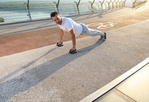 Full length portrait of a handsome middle aged Caucasian man, muscular build athlete doing push ups during an outdoor workout on the city bridge early in the morning