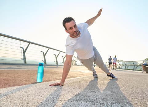 Middle aged European athlete sportsman doing push-ups, exercising on the glass city bridge at dawn. Bottle with water on the treadmill. Sport, active and healthy lifestyle concept