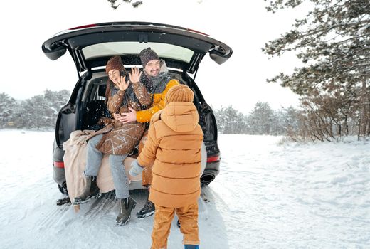 Lovely smiling couple sitting in car trunk in winter forest, close up