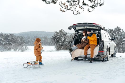 Winter portrait of a family sit on car trunk enjoy their vacation in snowy forest