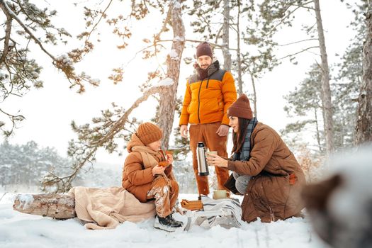 Happy family with cups of hot tea spending time together in winter forest, close up