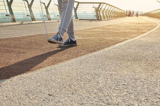 Sportsman during morning cardio workout with jumping rope on city bridge at dawn. Close-up of the legs of a male athlete exercising outdoors with a skipping rope. Motion, active and healthy lifestyle