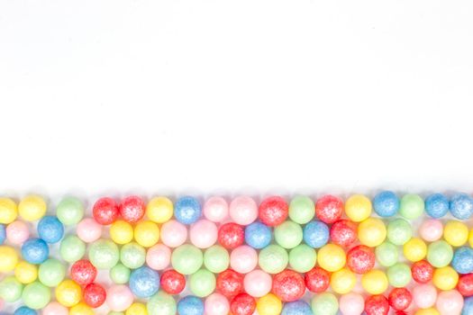 Multi-colored round glossy balls of sugar confectionery topping lie at the down on a white background.Copy space