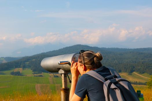 A girl looks through binoculars high in the mountains. Traveler