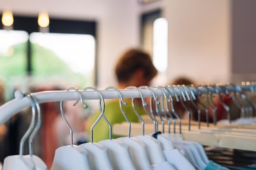 close up shot of a hang clothes in a fashion shop. clothes for sale, shopping concept. copy space. shopping concept. leisure concept. customers in the background walking. Natural light, sun rays, display, clothes rack, coloured clothes, horizontal view, copy space.