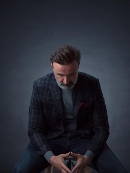 Portrait of adult businessman wearing trendy suit and sitting in modern studio on stylish chair against the black background. Horizontal mockup. High quality photo