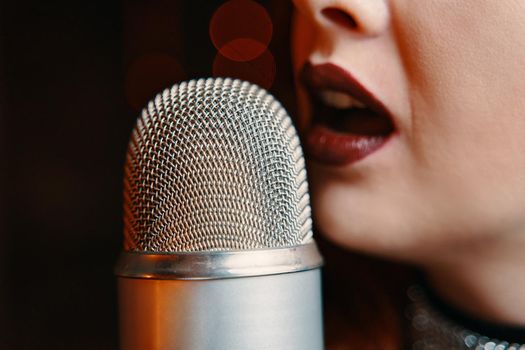 Woman singer with disco mic on bokeh light background. Copy space for gig posters. Close-up of female's lips painted with burgundy lipstick and retro microphone.