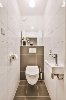 Interior of narrow restroom with sink and wall hung toilet with white walls and checkered floor