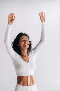 a female yogi in white clothes with her hands up meditates in the Yoga hall.