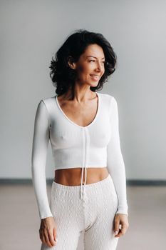 Portrait of a cheerful smiling woman in white sportswear, highlighted on a gray background.