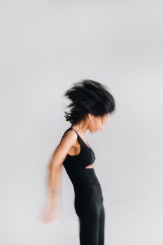 A blurry silhouette of a woman in black sportswear is engaged in dynamic kali meditation in the yoga hall.