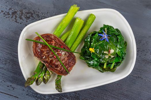 Top view of a grilled tournedos accompanied by spinach and asparagus.