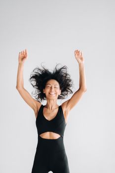 A blurry silhouette of a woman in black sportswear jumps up and raises her arms up against a white background.