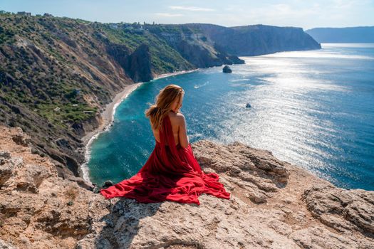 A girl with flowing hair in a long red dress sits on a rock above the sea. The stone can be seen in the sea