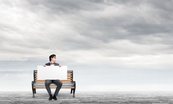 Young businessman holds a large white banner. sits on the bench