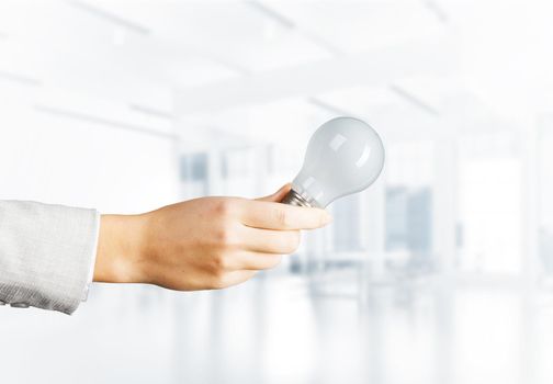 Human hand with incandescent lamp on blurred office background. Professional business assistance and consulting service. Successful solution business motivation with electric light bulb.