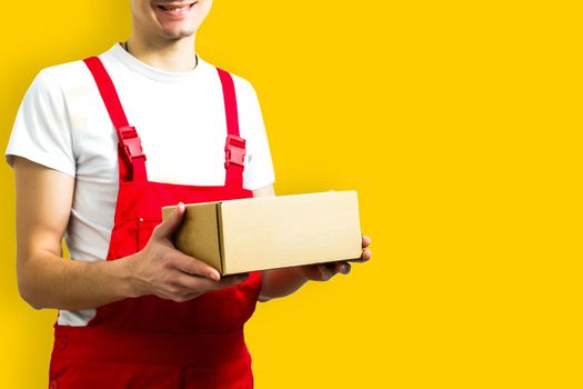 mage of a happy young delivery man in red cap standing with parcel post box isolated over yellow background