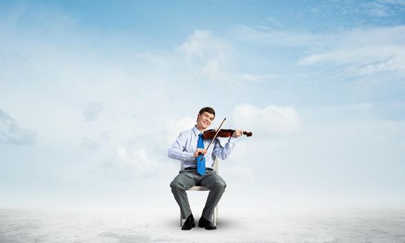 Young businessman plays the violin. enjoys music against the background of a blue sky with clouds