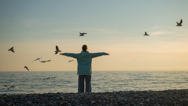 Caucasian woman spread her arms like wings on the seashore at sunset