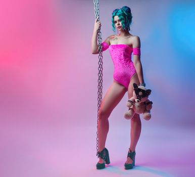 sexy girl with dyed hair in a bright pink bodysuit with a metal chain and soft toy on a neon background