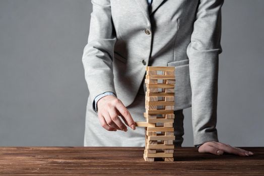 Businesswoman removing wooden block from tower on table. Management of risks concept with wooden jenga game. Business development and assistance. New challenge and leadership motivation.
