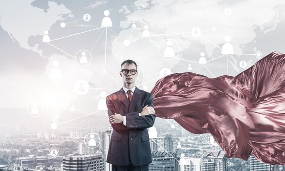 Young confident businessman wearing red cape against modern city background