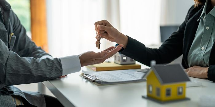 Real estate agent holding house key to his client after signing contract agreement in office,concept for real estate, moving home or renting property.
