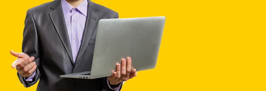 Working with joy. Handsome young man using his laptop and looking at camera with smile while standing against yellow background