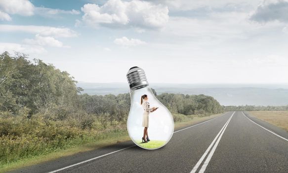 Young businesswoman trapped inside of light bulb on asphalt road
