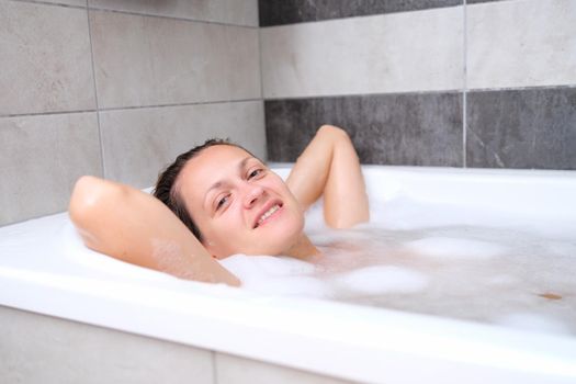 Smiling beautiful woman lies in a bath with foam. Relaxation and relaxation in the bathroom concept