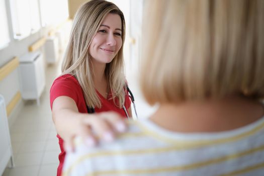 Smiling female doctor keeps hand on patient shoulder. Medical services and medical support concept