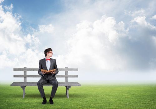 young student with a book. sits on a wooden bench