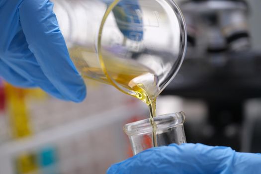 Chemical laboratory research and liquid oil processing. Scientist manually pouring yellow liquid from a chemical test tube into a glass flask concept