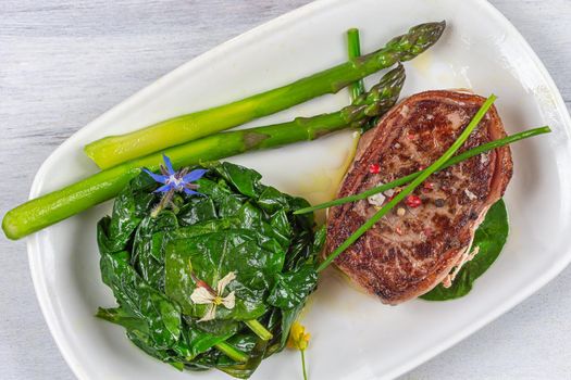 Top view of a grilled tournedos accompanied by spinach and asparagus.